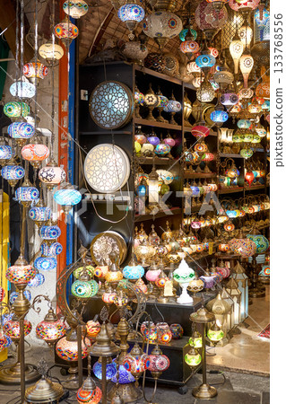 A vibrant shop displays an array of colorful, intricate mosaic lamps, radiating warmth and beauty in a bustling market. 133768556