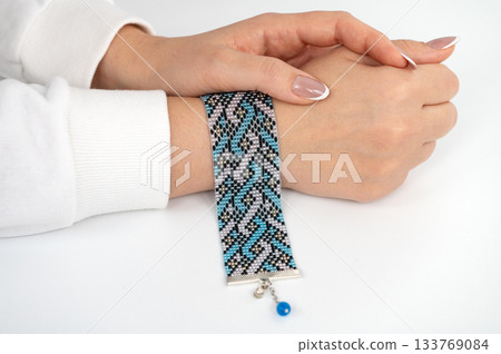 Female hand modeling intricate beaded bracelet with blue and black pattern 133769084