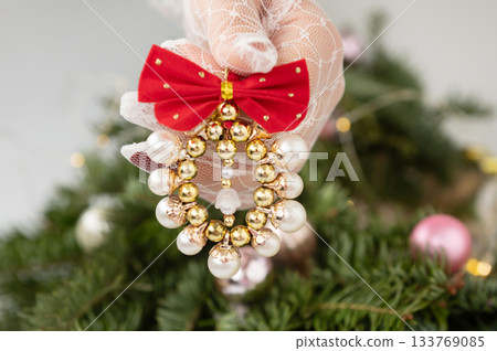 Elegant christmas ornament held by gloved hand against decorated tree background Elegant christmas ornament held by gloved hand against decorated tree background 133769085