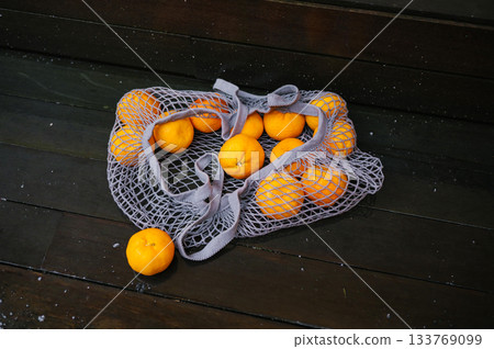 Fresh oranges in gray mesh bag on wooden floor 133769099