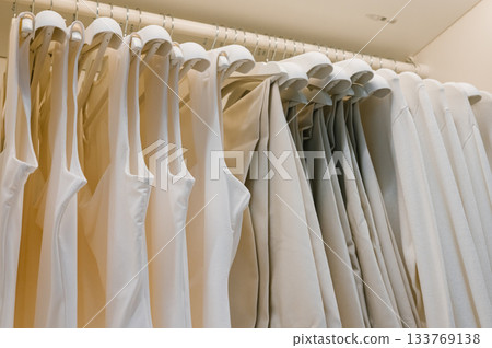 Organized wardrobe with neatly hung white and beige clothing Organized wardrobe with neatly hung white and beige clothing 133769138