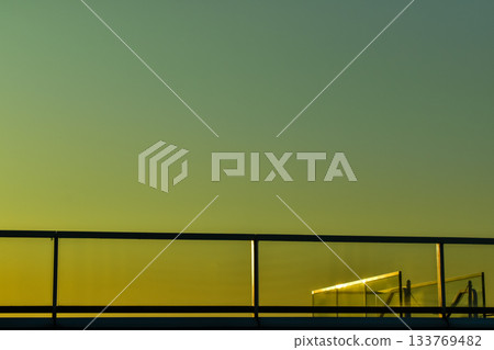 Balcony with sunset sky.  Glass architecture balcony on a park deck roof top with sunset light trough the transparent glass and warm color tones. Modern building design.  133769482