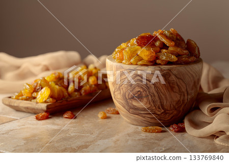Yellow sultana raisins in a wooden bowl on a beige background. 133769840