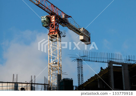 Control Cabin and Counterweight of Red Tower Crane at Construction Site. Monolithic Box with Window Holes and Rebar outlets against Blue Sky background. 133770918