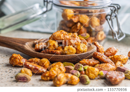 Nuts coated in sugar glaze on wooden spoon on kitchen table. 133770936