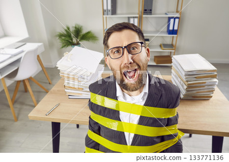 Angry stressed business man tied on his workplace in office shouting with shocked face expression. 133771136