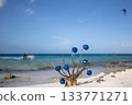 Dead corals decorated with blue Christmas balls standing on the sand beach with blue sea behind it, with a kitesurfer away.  133771271