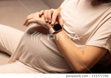 Pregnant woman with watches. Pregnant woman looking at her watches. 133771798