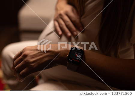 Pregnant woman measuring heart rate with her watches. Pregnant woman measuring heart rate with her watches. 133771800