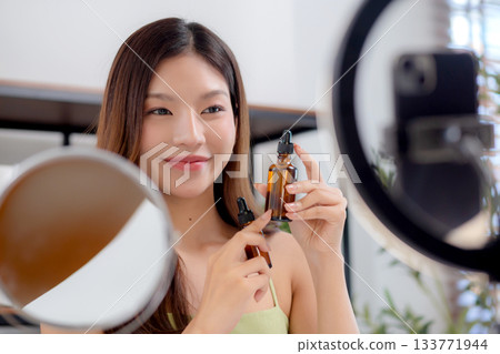 Young asian woman demonstrating serum on hands on social media at home. Young asian woman demonstrating serum on hands on social media at home. 133771944