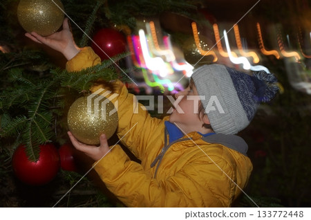 Child Hanging Ornaments on Christmas Tree at Night Child Hanging Ornaments on Christmas Tree at Night 133772448