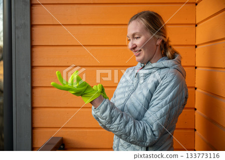 woman putting on green cleaning gloves on outdoor balcony 133773116