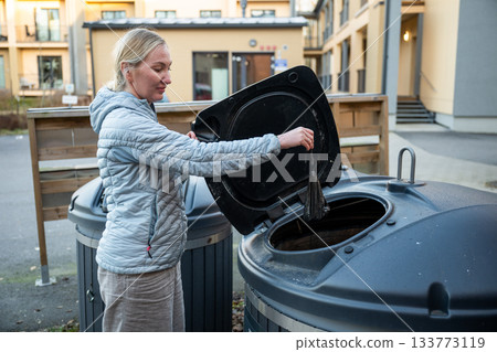 woman disposing waste bag into outdoor recycling bin in residential area woman disposing waste bag into outdoor recycling bin in residential area 133773119