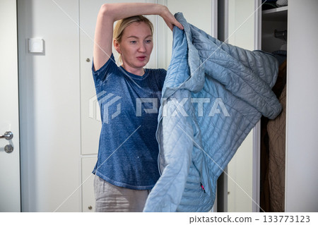 Woman putting on blue jacket in home wardrobe Woman putting on blue jacket in home wardrobe 133773123