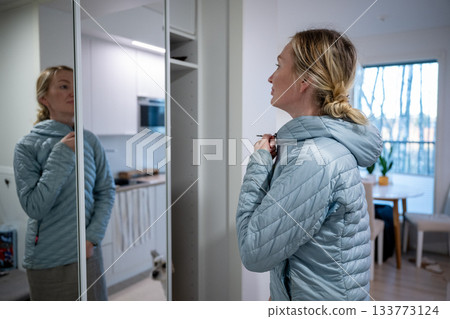 Woman putting on blue jacket in home wardrobe Woman putting on blue jacket in home wardrobe 133773124