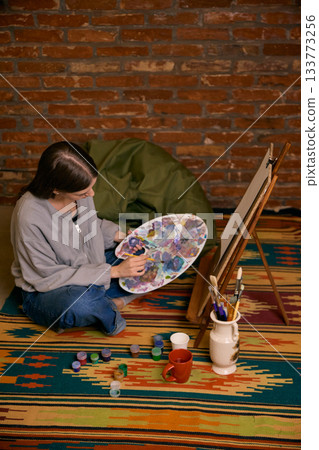 Woman mixing paint palette during relaxed home art practice 133773256