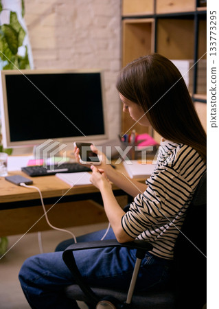 Young woman checking smartphone while studying at desk 133773295