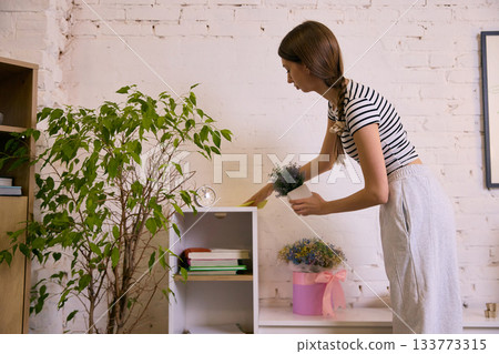 Young woman organizing home shelf and placing decor plant 133773315