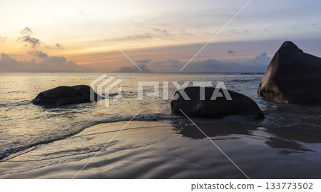 A tranquil coastal scene at dusk features gentle waves and golden reflections 133773502