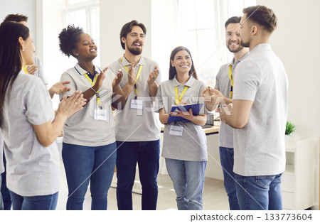 Volunteers standing indoors, smiling and applauding finishing work in charity donation center 133773604