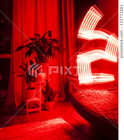 A long-exposure photograph that captures the pathway of a moving red light source in a dimly lit room 133773881