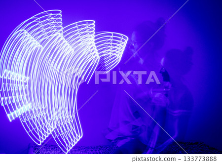 A long-exposure photograph that captures the pathway of a moving blue light source in a dimly lit room 133773888