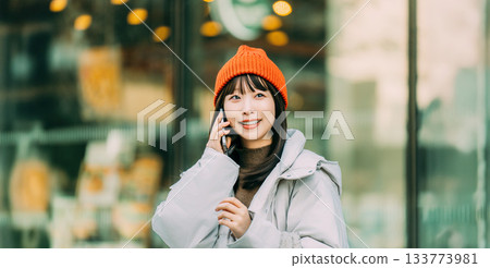 冬日街角,一位微笑的女子正在使用智慧型手機。 冬日街角,一位微笑的女子正在使用智慧型手機。 133773981