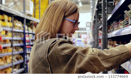 Customer making purchasing decisions, carefully examining goods on shelves in grocery store, navigating abundance of options with focus and attention to detail Customer making purchasing decisions, carefully examining goods on shelves in grocery store, navigating abundance of options with focus and attention to detail 133774669