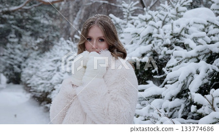 Elegant blonde woman wearing luxurious white fur coat, standing amid snowy forest landscape, experiencing peaceful winter scenery with graceful composure 133774686