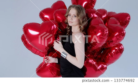 Elegant woman wearing black dress, standing with red heart shaped balloons, expressing romantic mood and festive valentine's spirit 133774692