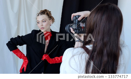 Fashion photographer taking pictures of a beautiful model wearing red gloves and a red flower choker, posing in a studio with black and white background Fashion photographer taking pictures of a beautiful model wearing red gloves and a red flower choker, posing in a studio with black and white background 133774717