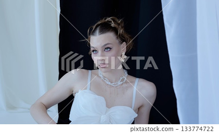 Professional fashion model showcasing a stylish white top and delicate jewelry, creating a sophisticated and glamorous look against a contrasting black and white backdrop 133774722