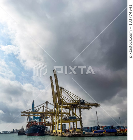 Massive Gantry Cranes and Container Ship Under Dramatic Sky Massive Gantry Cranes and Container Ship Under Dramatic Sky 133774941