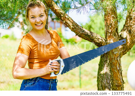 Female cuts branches of tree, using saw Female cuts branches of tree, using saw 133775491