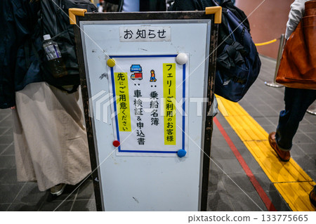 A Japanese notice board guiding passengers through ferry boarding procedures and passengers waiting 133775665
