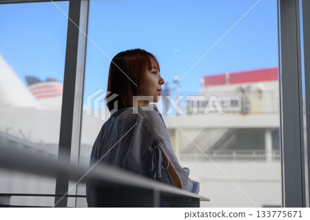 一位年輕女子站在窗邊，凝視著窗外，她的身影若隱若現。 133775671