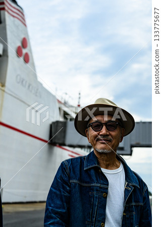Smiling elderly man wearing a hat with a ferry in the background Smiling elderly man wearing a hat with a ferry in the background 133775677