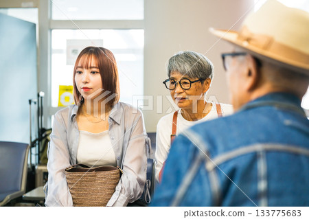 年輕女子在醫院候診室與一對老年夫婦交談 133775683