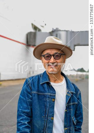 一位面帶微笑的日本老先生,身穿牛仔夾克,頭戴牛仔帽,站在一艘船前。 一位面帶微笑的日本老先生,身穿牛仔夾克,頭戴牛仔帽,站在一艘船前。 133775687
