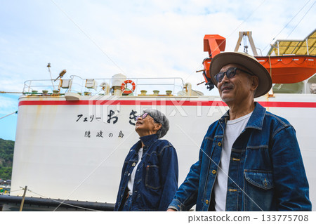 A senior Japanese couple wearing denim jackets standing with a ferry in the background A senior Japanese couple wearing denim jackets standing with a ferry in the background 133775708