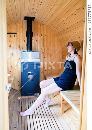 Young woman relaxing in a barrel sauna Young woman relaxing in a barrel sauna 133775715