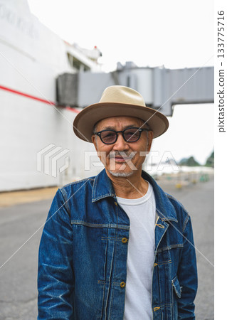 A middle-aged Japanese man wearing a denim jacket and hat waiting to board a ferry A middle-aged Japanese man wearing a denim jacket and hat waiting to board a ferry 133775716