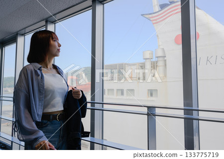 一位年輕女子正等船，她望著窗外的港口。 133775719