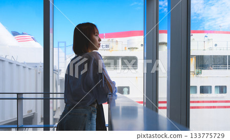 Young woman looking out the window at the ships at the harbor Young woman looking out the window at the ships at the harbor 133775729