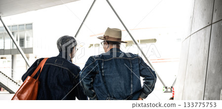 兩名身穿牛仔夾克的男子，背對著鏡頭，從一座現代建築內向外望去。 133775753