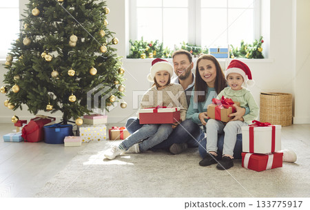 Happy family with children sitting under Christmas tree with many present gift boxes Happy family with children sitting under Christmas tree with many present gift boxes 133775917