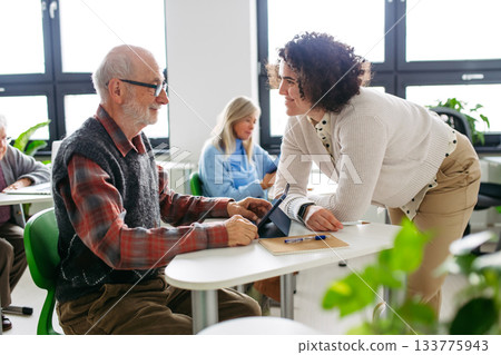 Senior man learning digital skills with tutor support in community center. Senior man learning digital skills with tutor support in community center. 133775943