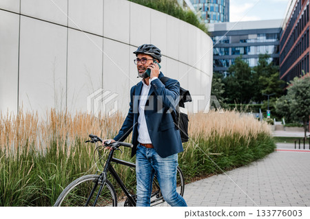 Cyclist making phone call, standing on streeet. 133776003