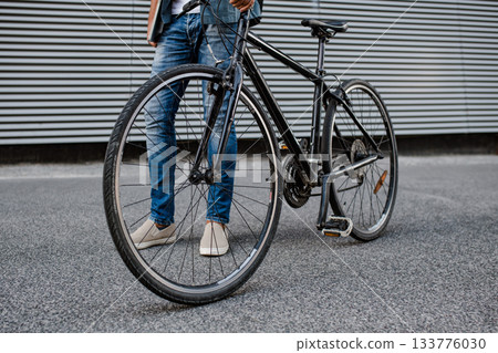 City commuter riding bike on street, holding ball and headphones. 133776030