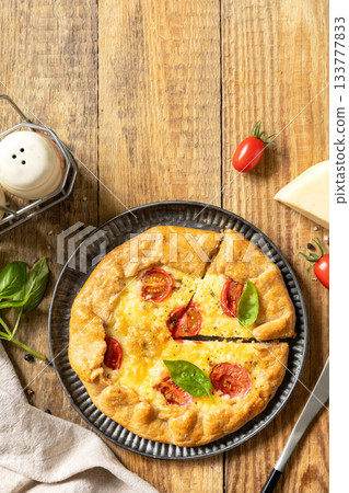 Crispy tomato galette with adyghe cheese and herbs on rustic background. Top view. Crispy tomato galette with adyghe cheese and herbs on rustic background. Top view. 133777833